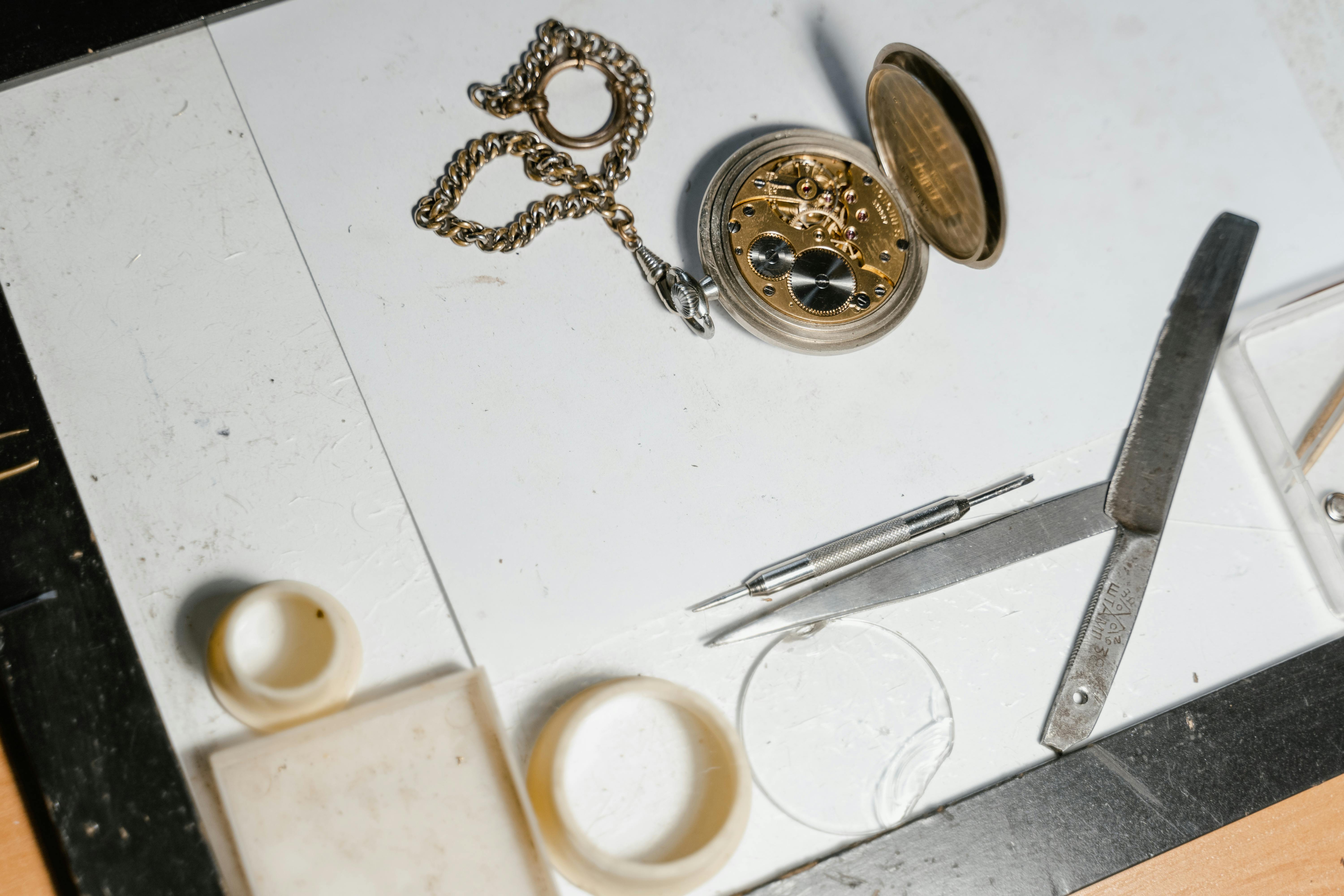 Opened pocket watch with case back removed, showing the movement alongside repair tools on a workbench